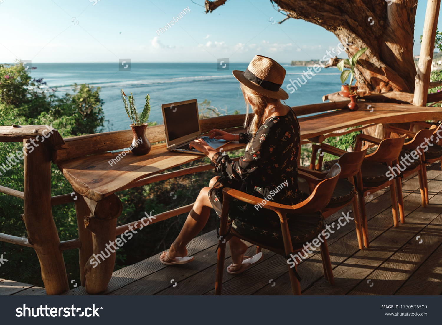 Freelance concept. Pretty young woman using laptop in cafe on tropical beach in outdoor cafe terrace with sea view. Work and travel
