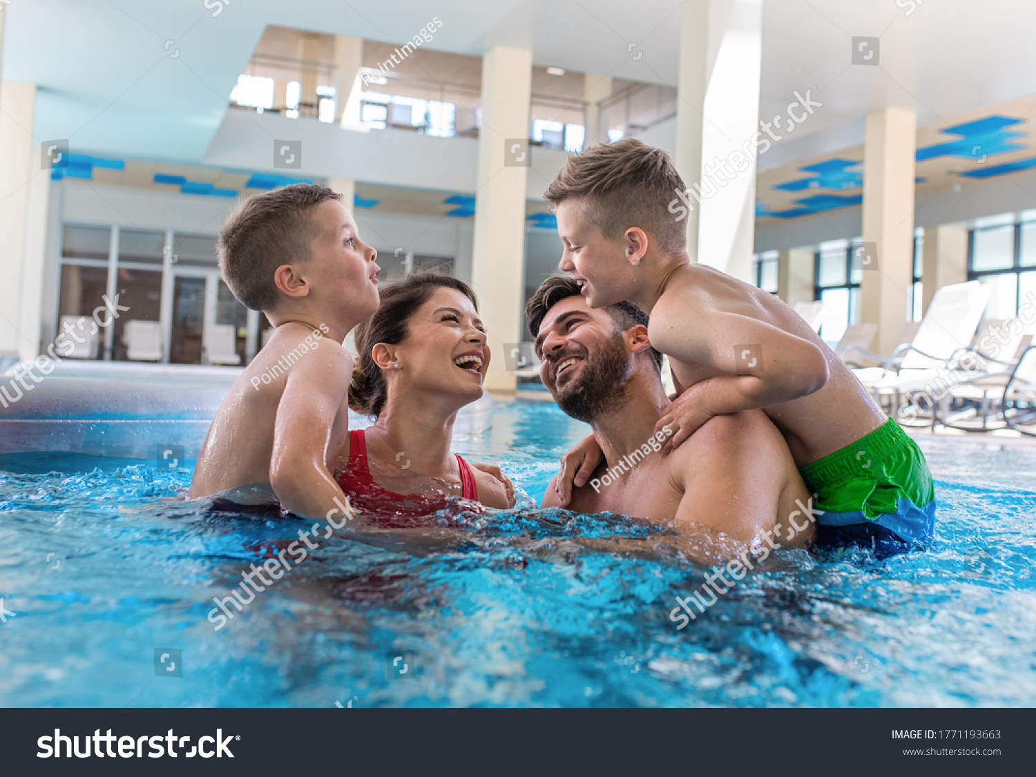 Smiling family of four having fun and relaxing in indoor swimming pool at hotel resort. #1771193663
