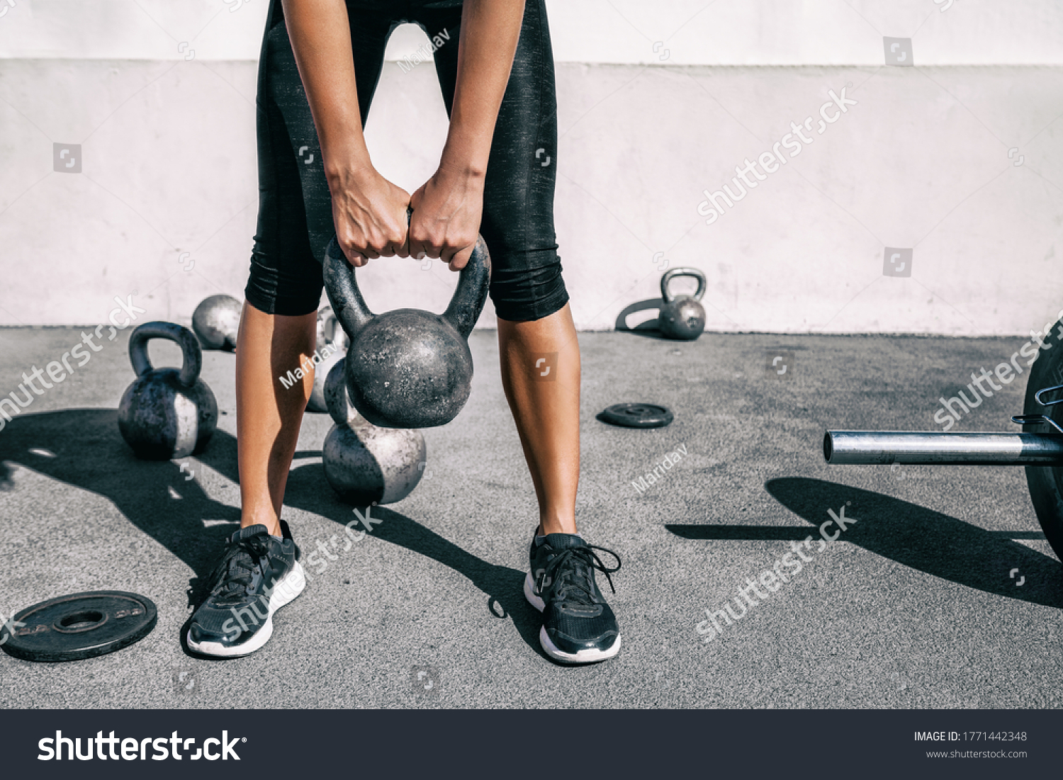 Kettlebell weightlifting athlete woman lifting weight at outdoor fitness gym. Lower body legs and feet closeup of strength training legs, glutes and back lifting free weights. #1771442348