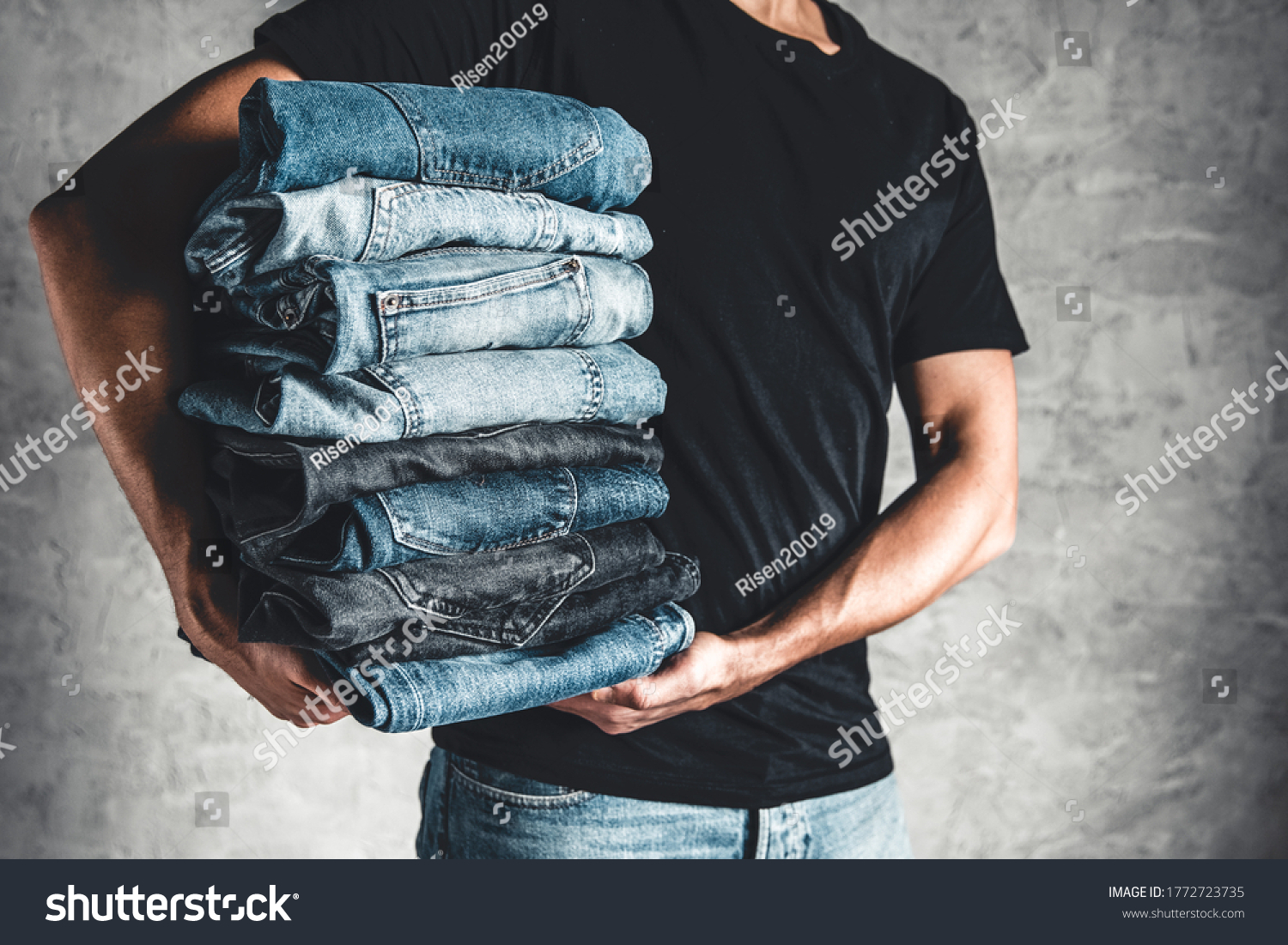 close up stack of folded denim blue jeans in hand over gray wall background, copy space #1772723735