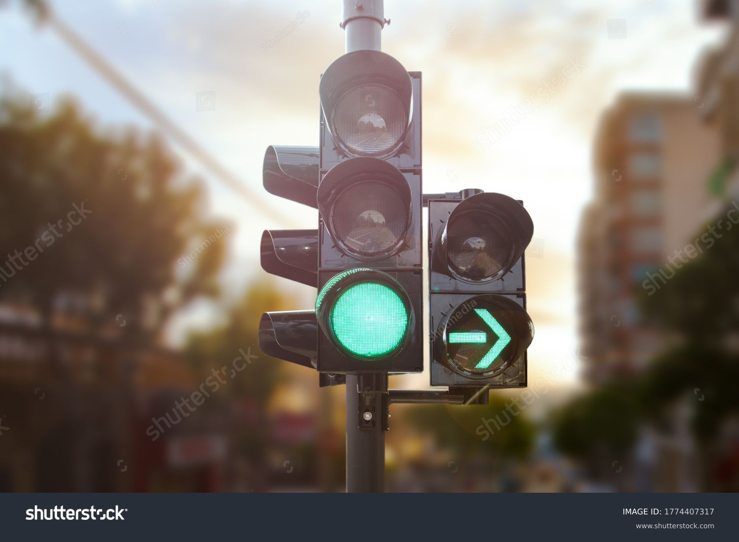Green traffic light with green arrow light up in city while sunset allows car to turn right #1774407317