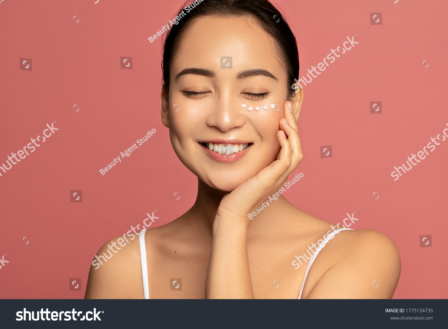 Anti aging eye cream. Young Beautiful model posing aginst pink background with applyed cream under her eyes #1775134739