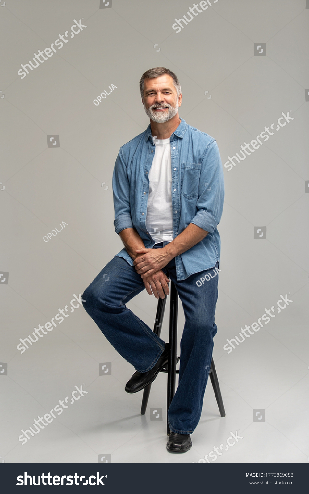 Portrait of a casual senior sitting on a chair on white background. #1775869088