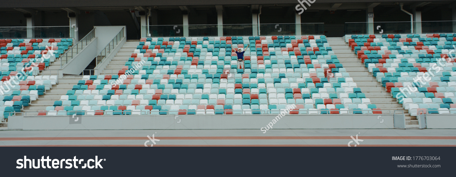WIDE view of a lonely fan spectator attending a sports event on an empty stadium. Isolation, events during coronavirus pandemic concept #1776703064