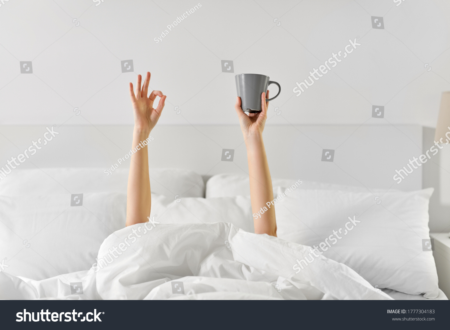 morning, comfort and people concept - young woman with cup of coffee lying in bed and showing ok hand sign at home bedroom #1777304183