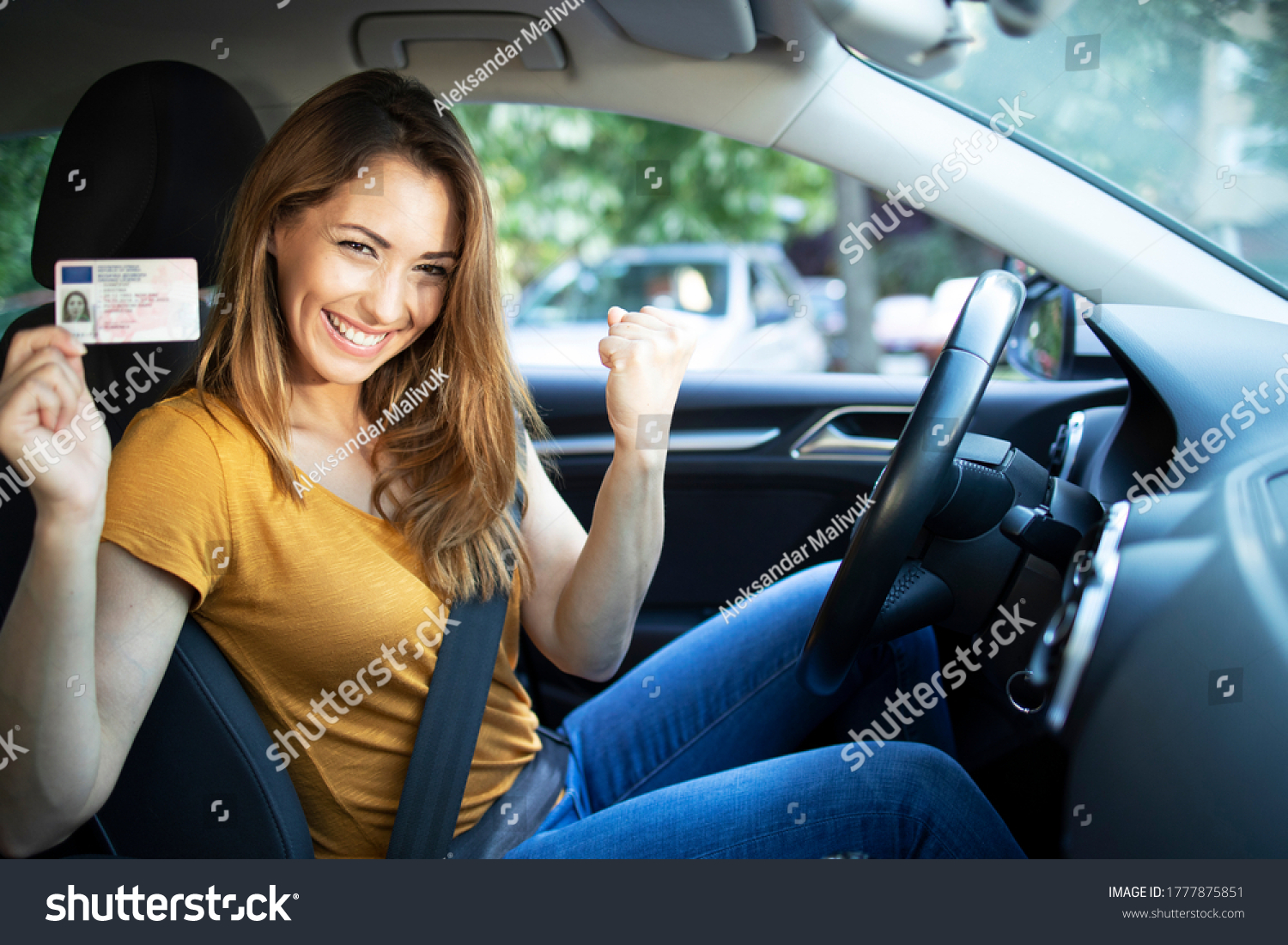 Car interior view of woman with driving license. Driving school. Young beautiful woman successfully passed driving school test. Female smiling and holding driver's license. #1777875851