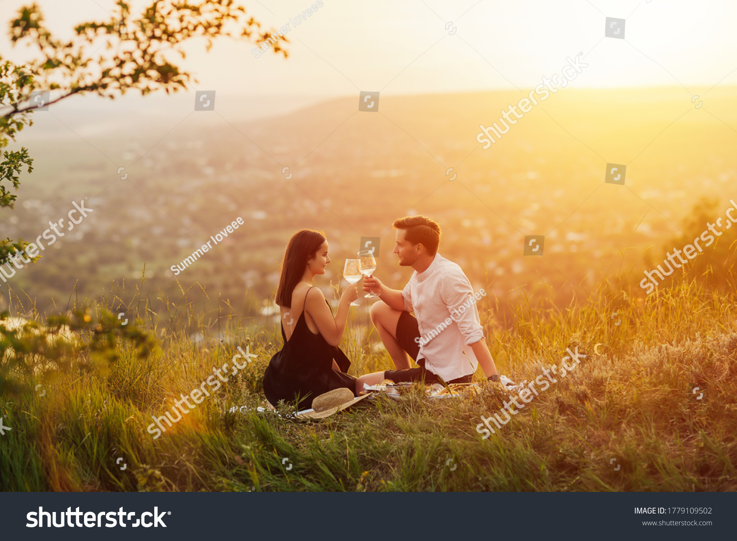 Couple in love on a white plaid take a picnic against the backdrop of a sunset in the mountains. Romantic time. Beautiful couple is enjoying picnic time at sunset.  Copy space. #1779109502