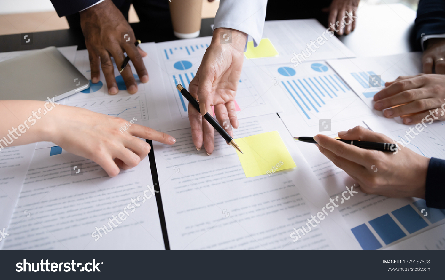 Diverse corporate staff discuss report shown in charts and graphs, analyzing financial stats, involved in project overview, reviewing results, close up. Employees participate in brainstorming concept #1779157898