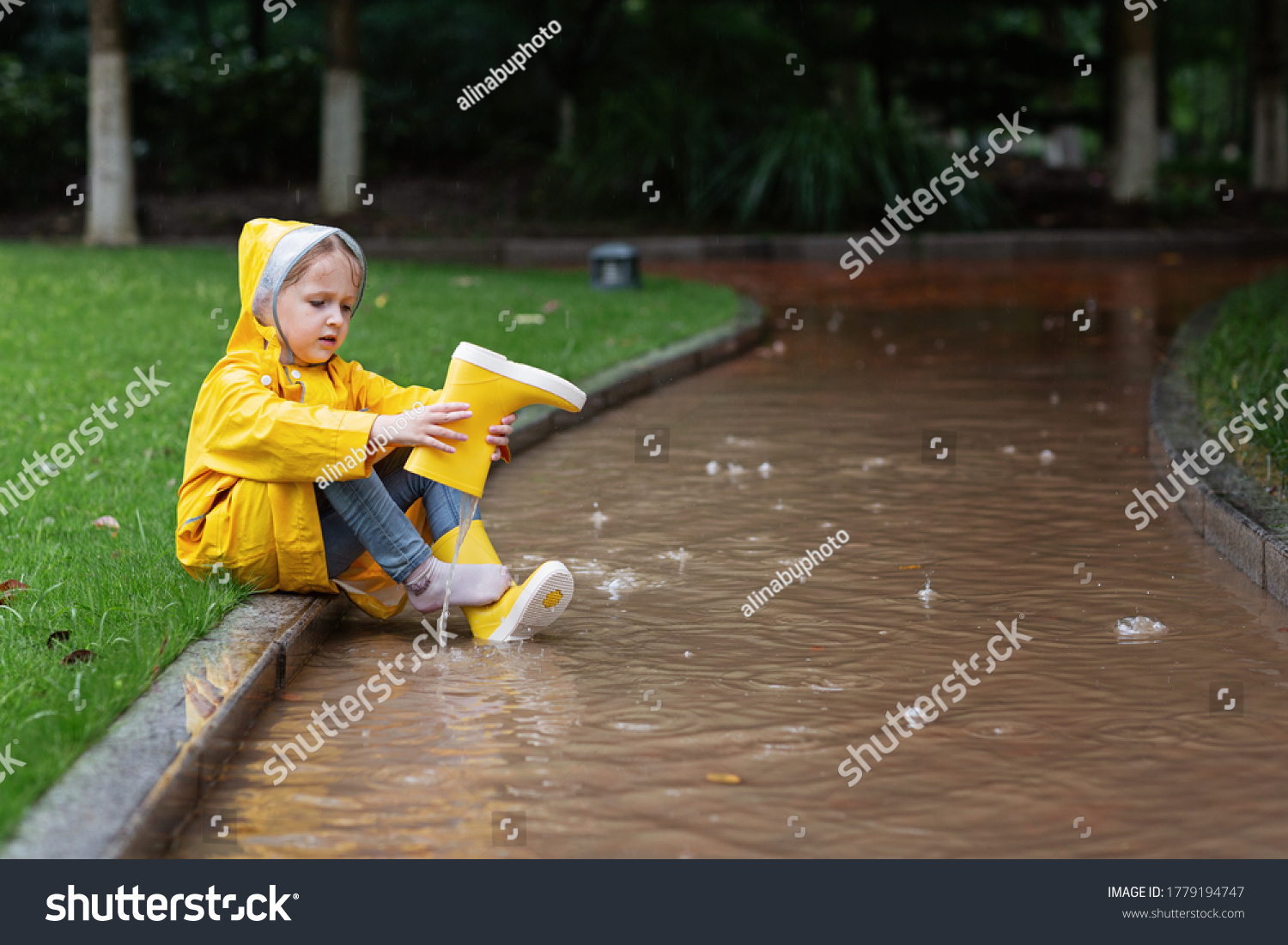 Cute little girl in yellow raincoat and rubber boots walking outdoor during rain. Bad weather, summer tropical storm, autumn fashion concept. #1779194747