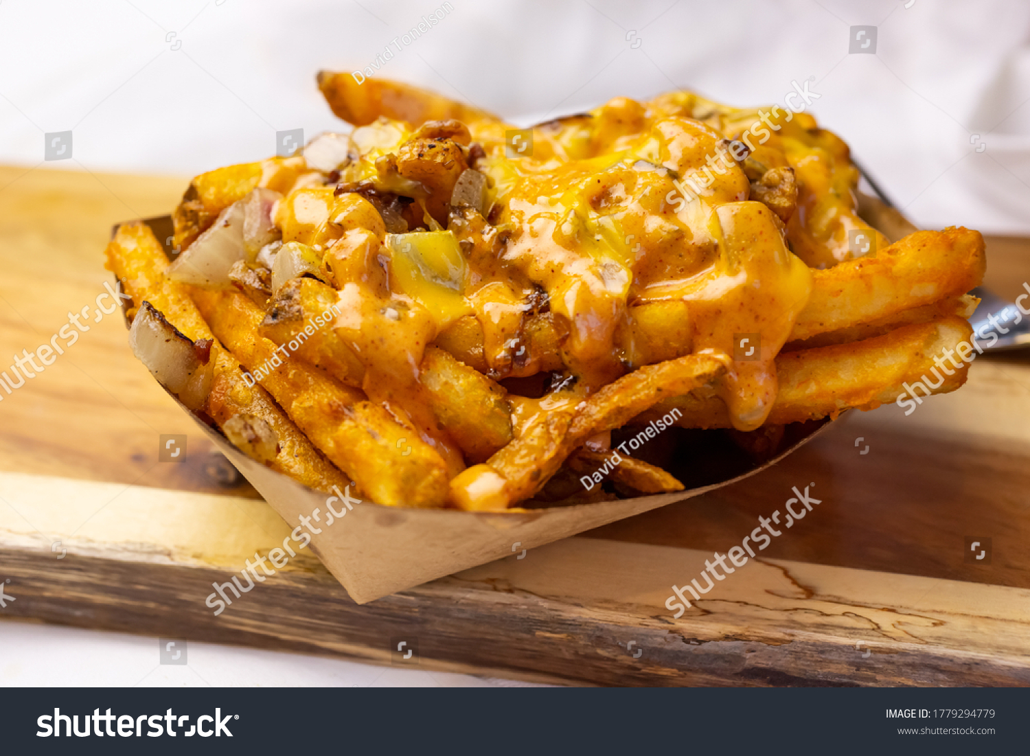 A view of a basket of loaded fries, on a wooden cutting board. #1779294779