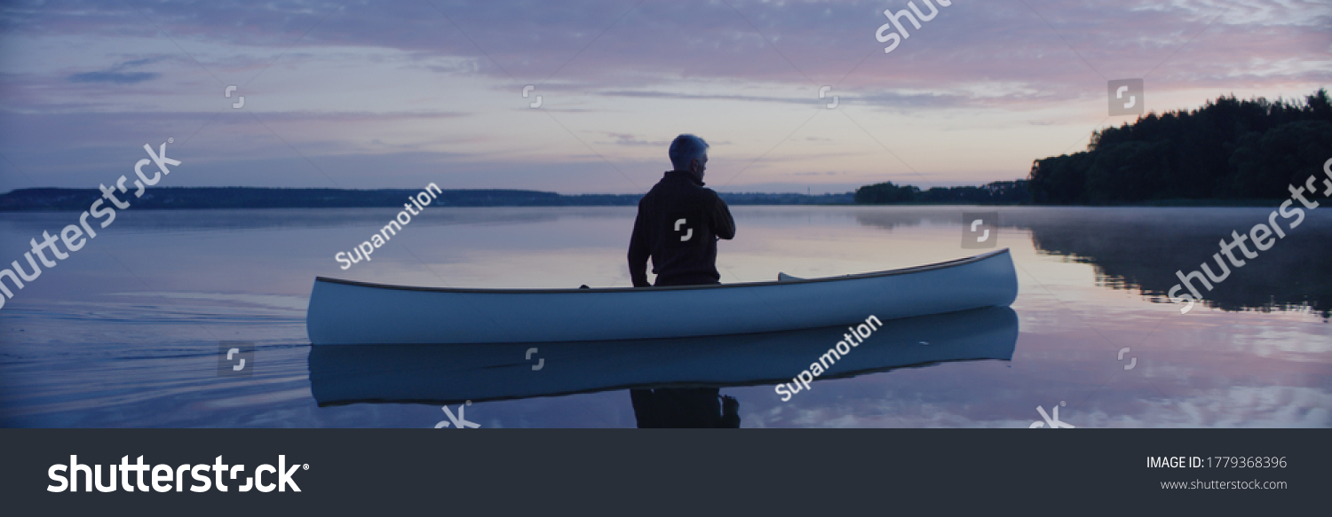 Man canoeing in a traditional wooden boat on a large lake at dawn #1779368396
