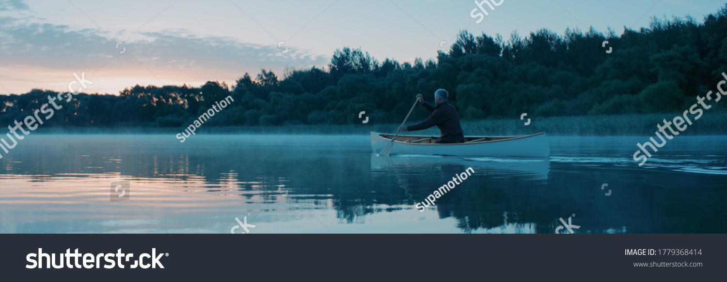 Man canoeing in a traditional wooden boat on a large lake at dawn #1779368414