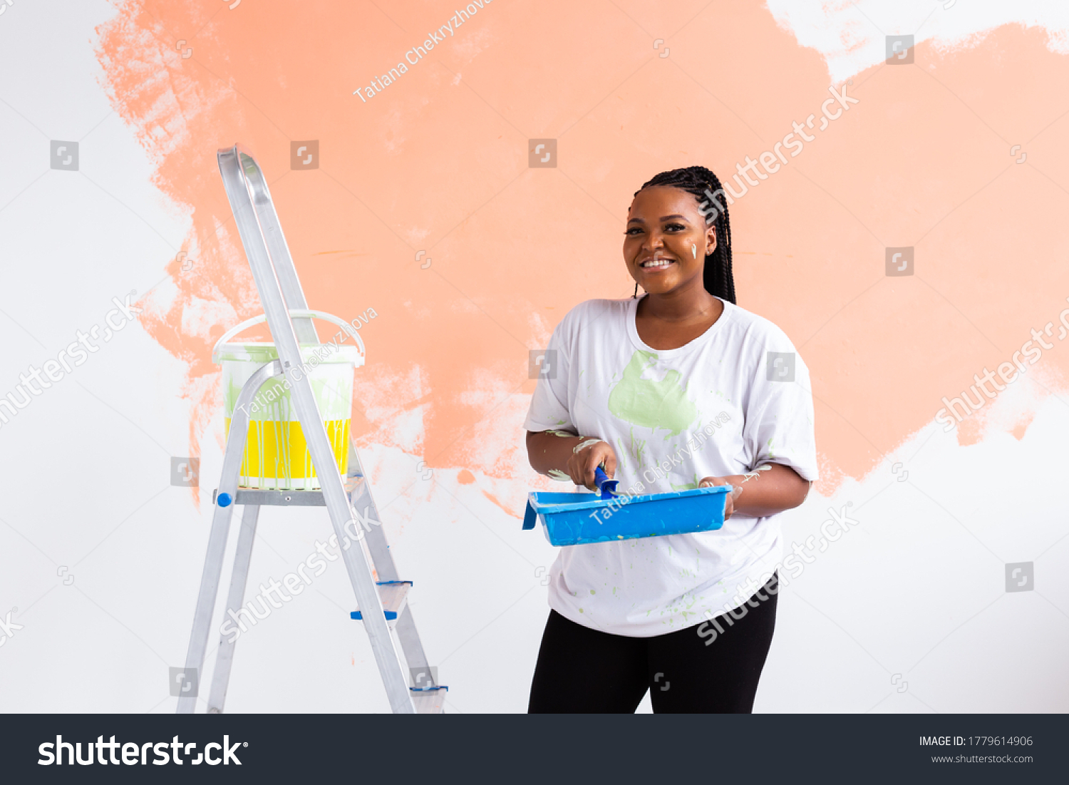 Beautiful african american girl painting the wall with paint roller. Portrait of a young beautiful woman painting wall in her new apartment. Redecoration and renovation concept. #1779614906