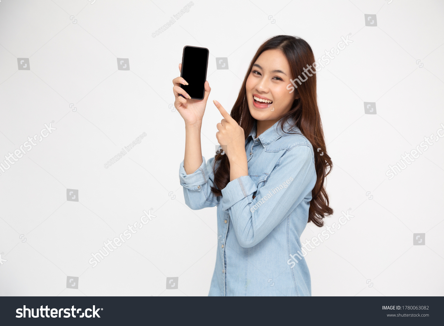 Portrait of Asian woman showing or presenting mobile phone application and pointing finger to smartphone on hand isolated over white background, Asian Thai model #1780063082