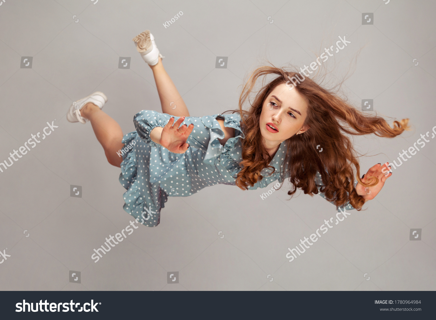 Beautiful girl levitating in mid-air, falling down and her hair messed up soaring from wind, model flying hovering with dreamy peaceful expression. indoor studio shot isolated on gray background #1780964984