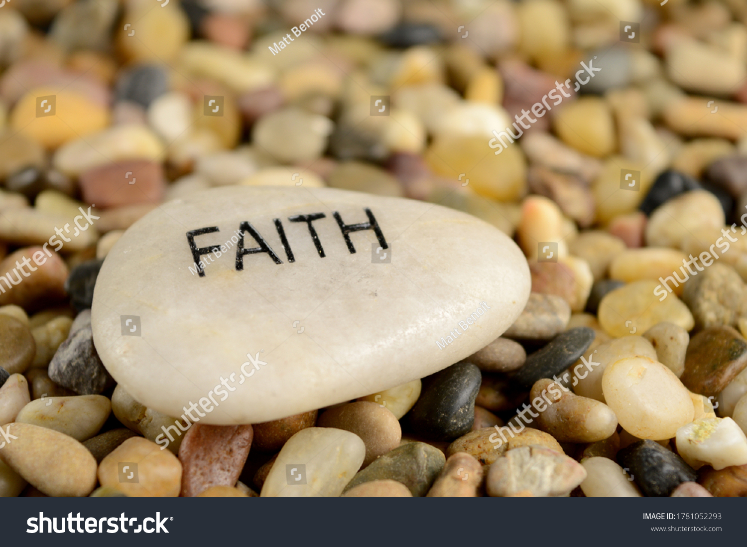 A smooth river stone is etched with the word faith for spiritual affirmation purposes. #1781052293