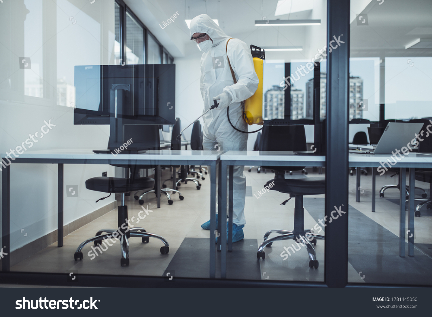 Office disinfection during COVID-19 pandemic. Man in protective suit and face mask spraying for disinfection in the office #1781445050