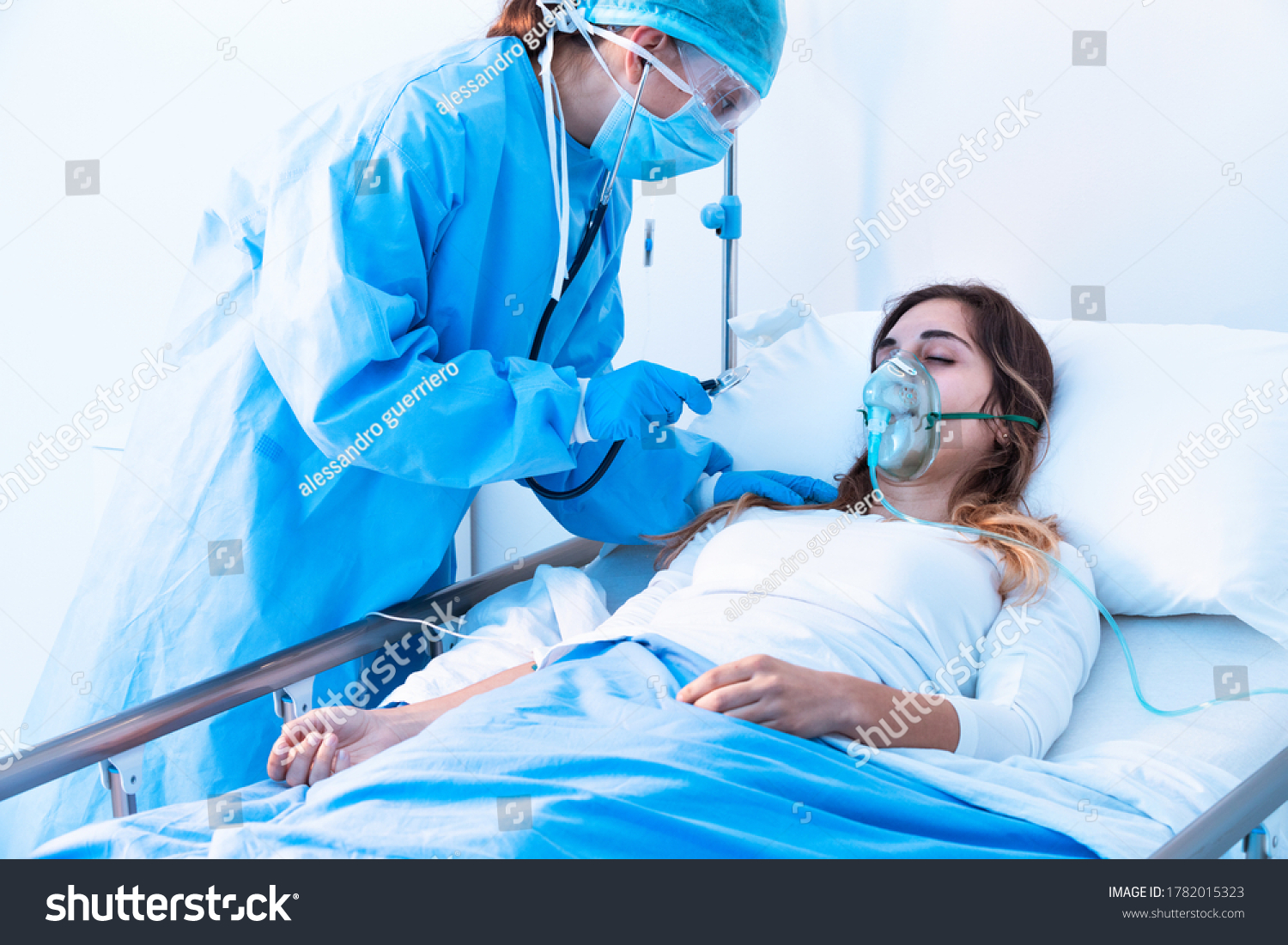 Doctor examining female patient in critical health conditions using a stethoscope in the intensive care unit of a modern hospital during covid-19 pandemic #1782015323