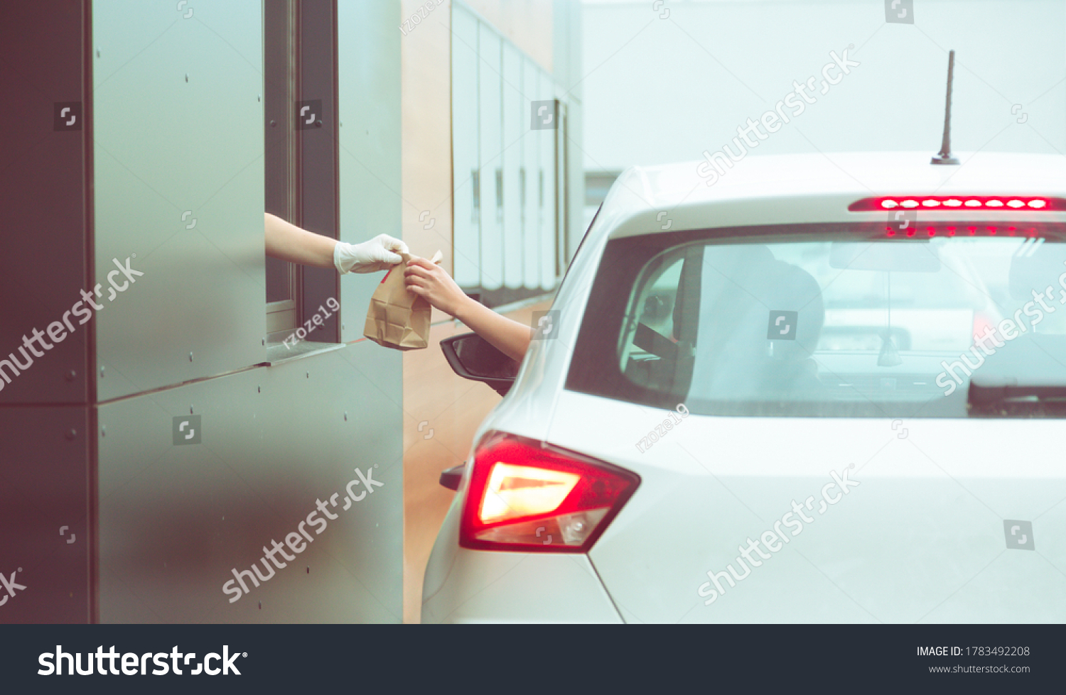 Employee wearing gloves delivers take out food out the window. Shopping for food from the car. Pick up fast food from the counter. Concept of social distance and new normality. #1783492208