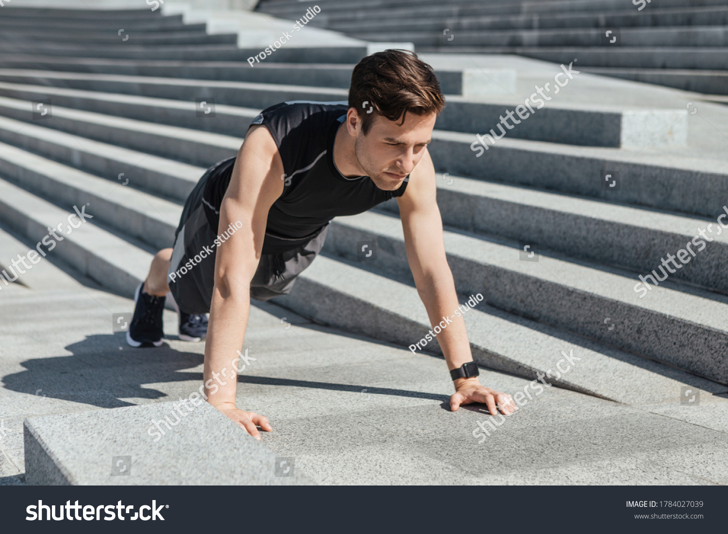 Active leisure and motivation. Millennial guy in sportswear with fitness tracker push up the city stairs at sunlight, free space #1784027039