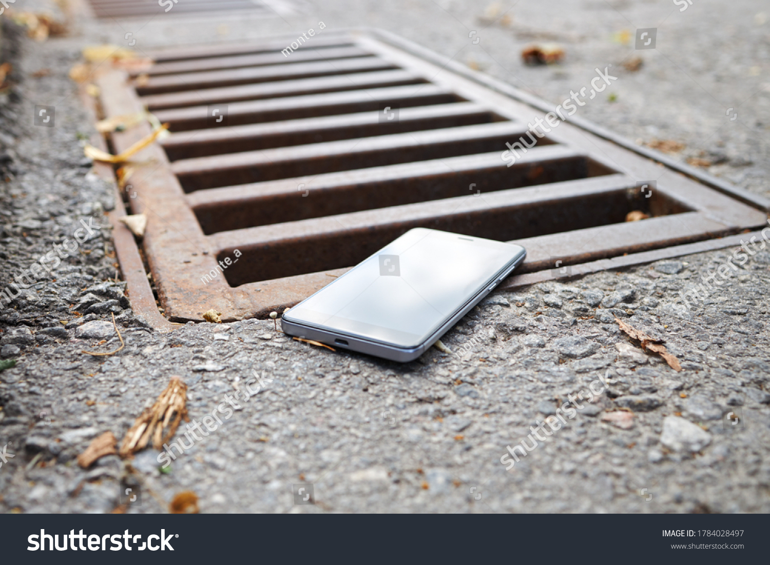 lost smart phone device laying on the ground near rain drain at city street.  #1784028497
