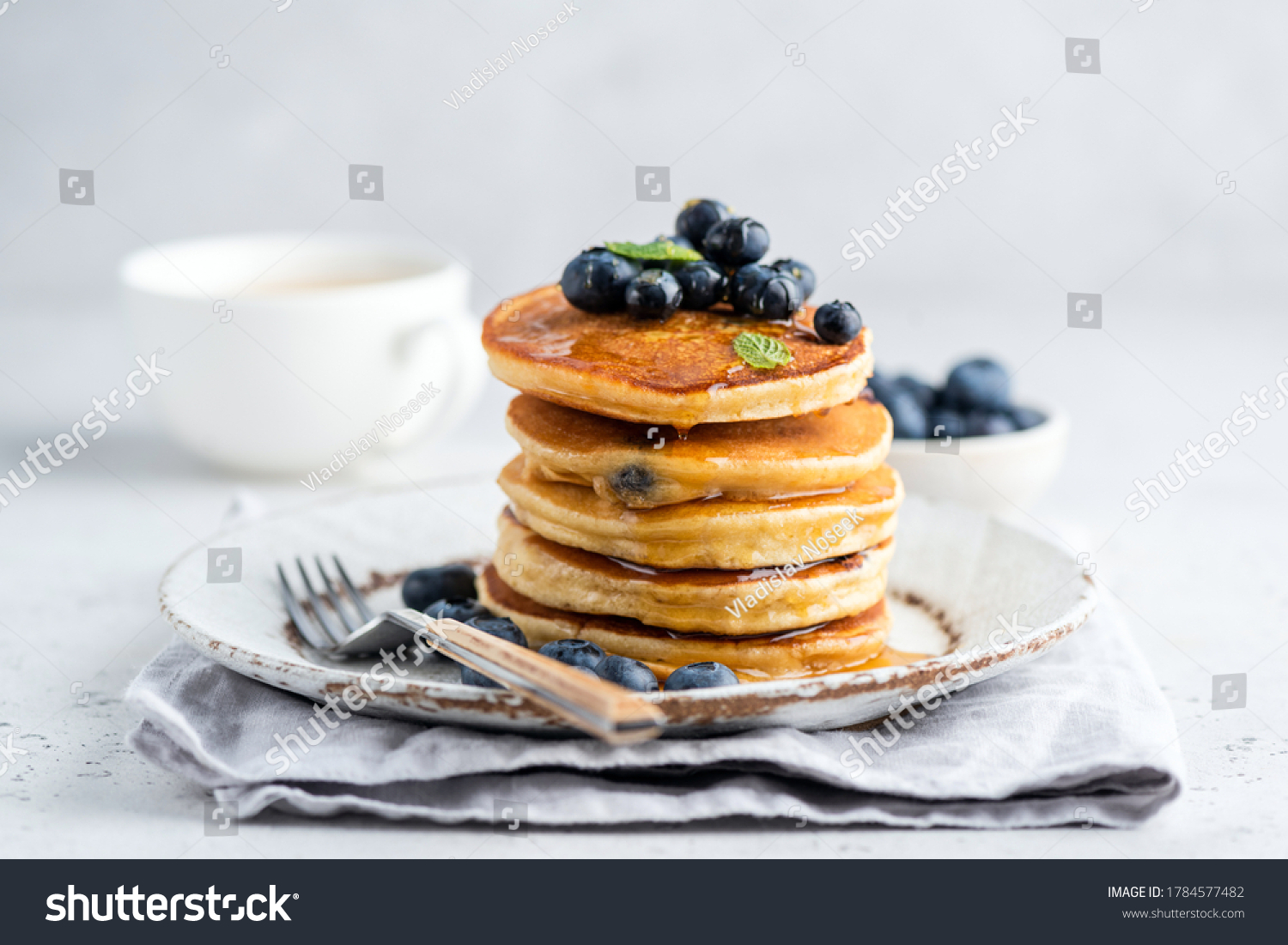 Tasty pancakes with blueberries and honey on a plate. Grey background #1784577482