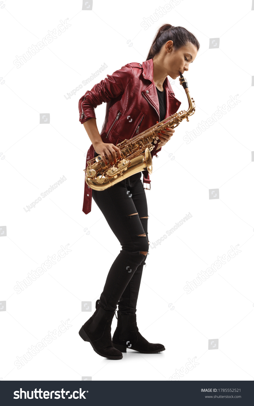 Full length profile shot of a young woman in a leather jacket playing a saxophone isolated on white background #1785552521