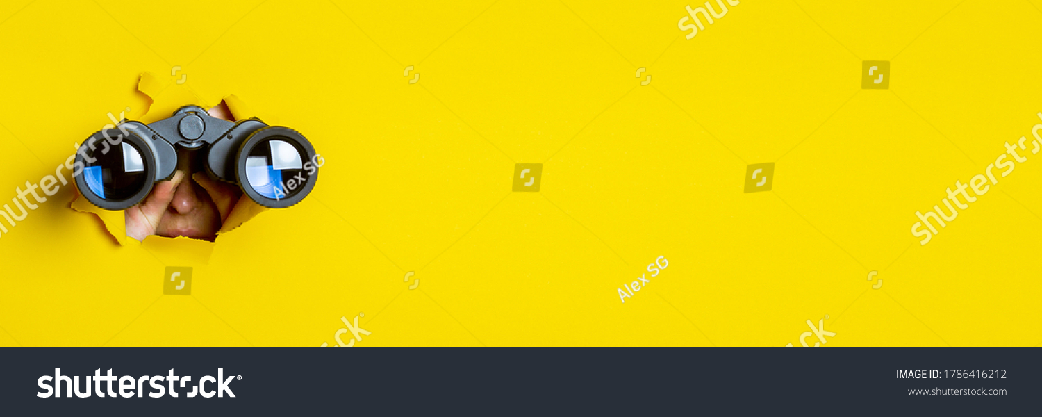 Female hand holds black binoculars on a yellow background. Journey, find and search concept. Banner. #1786416212