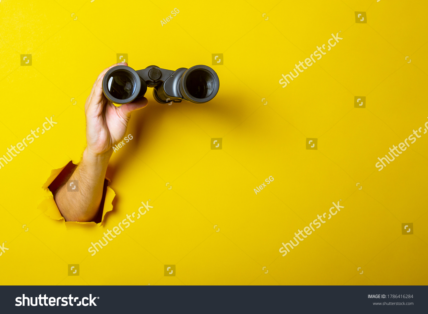 Female hand holds black binoculars on a yellow background. Looking through binoculars, journey, find and search concept #1786416284