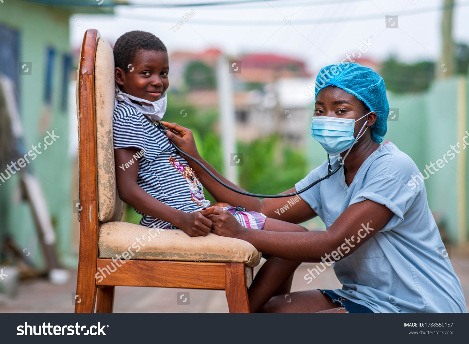 African health worker wearing a surgical face mask and child wearing homemade mask for protection,auscultating child chest,both looking at camera-concept on child health in covid-19 pandemic #1788550157
