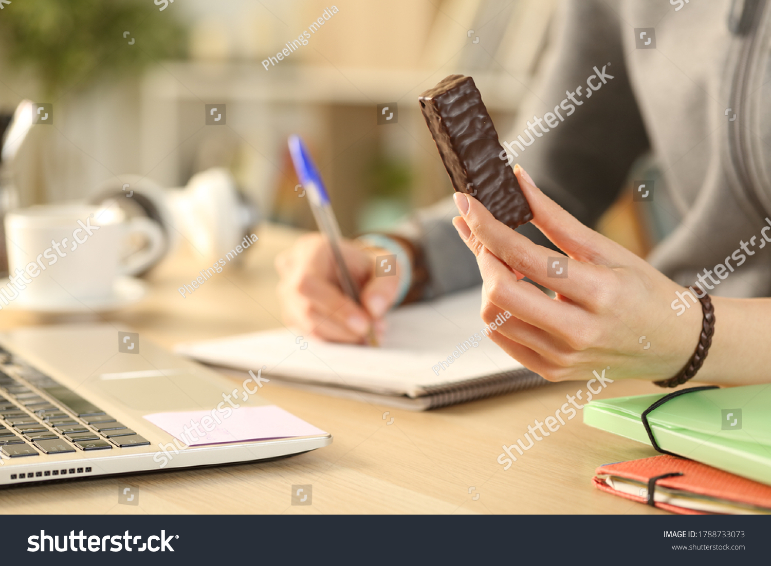 Close up of student girl hands holding chocolate snack bar studying at home #1788733073