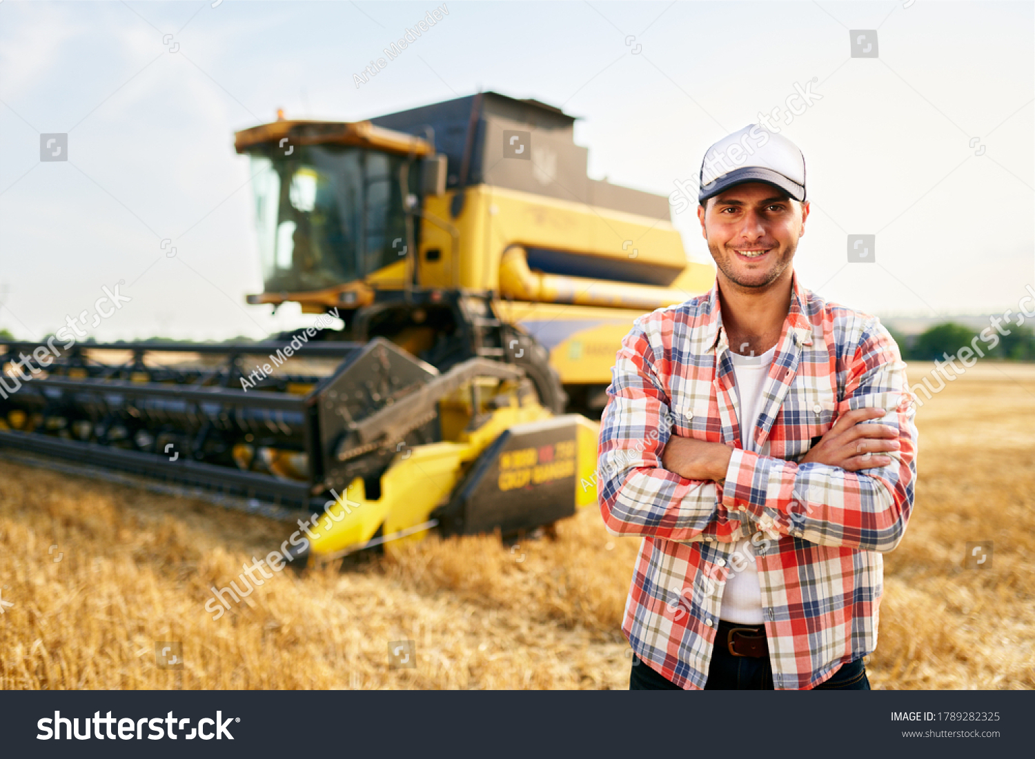 Portrait of proud harvester machine driver with hands crossed on chest. Farmer standing at his combine. Agronomist looking at camera. Rancher at harvesting work on stubble of harvested wheat field. #1789282325