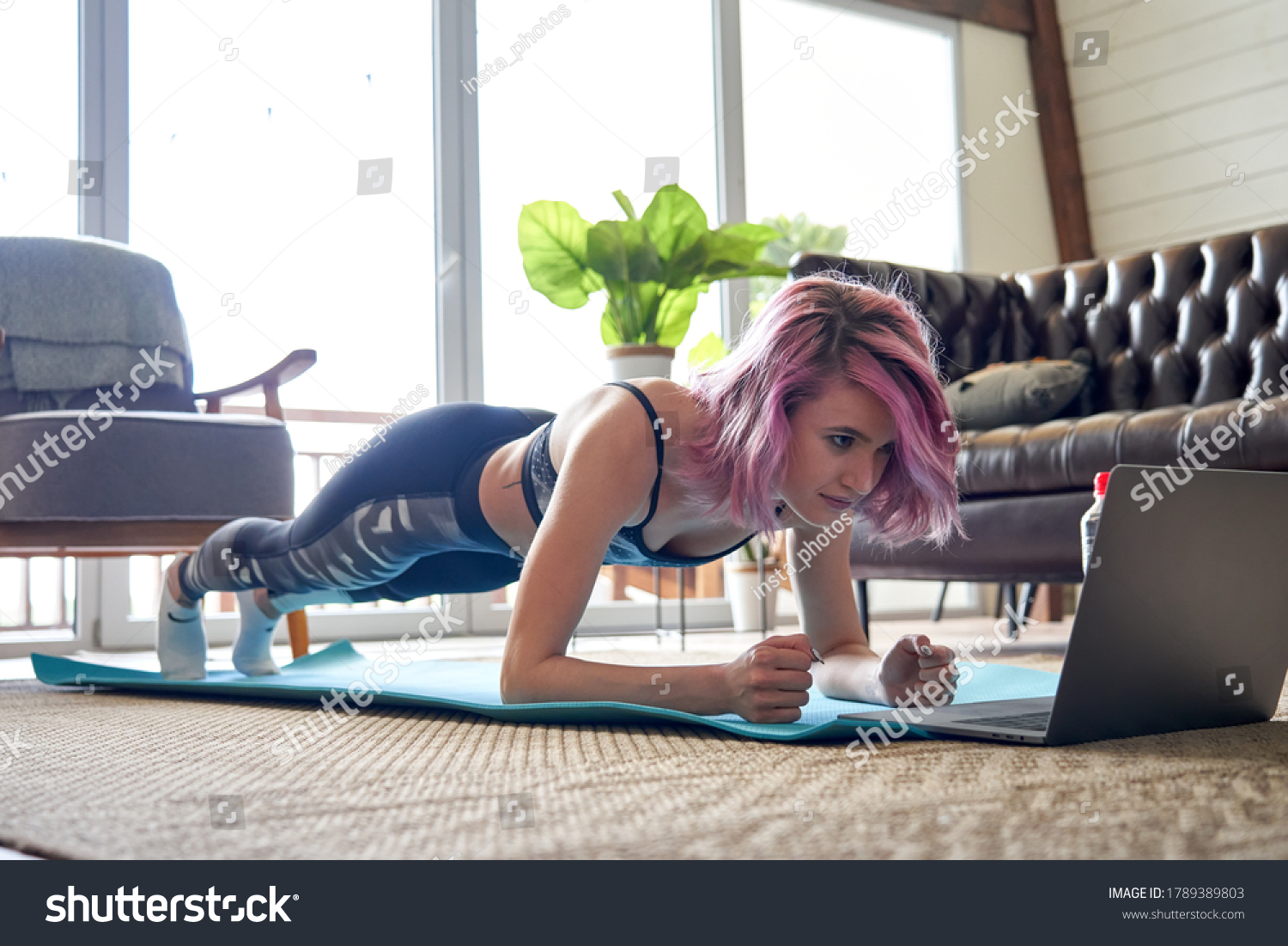 Young healthy sporty fit woman with pink hair wear sportswear doing plank sport training exercise watching online class tutorial on laptop at home. Online fitness workout video virtual coach concept. #1789389803