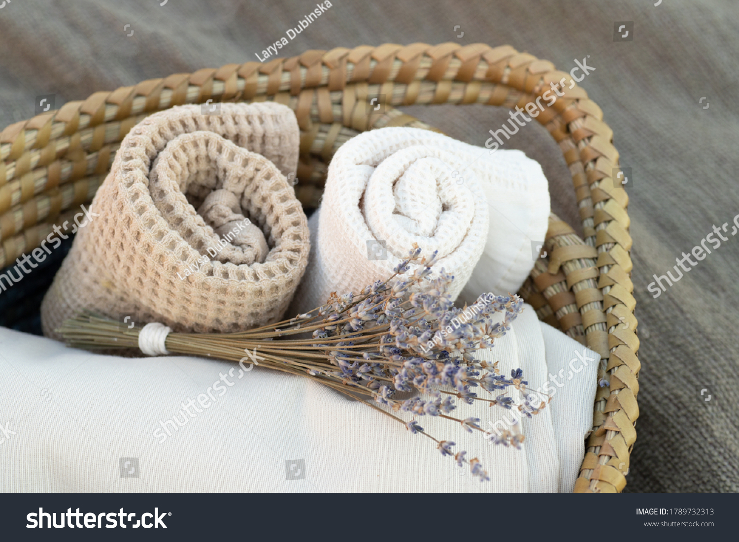 Home textiles. Natural fabric towels. Rolled towel, folded beige cloth, lavender bouquet in a basket. Close up. Nobody. Horizontal. Concept for smells, bathroom, spa, country, clothings, bath decor. #1789732313