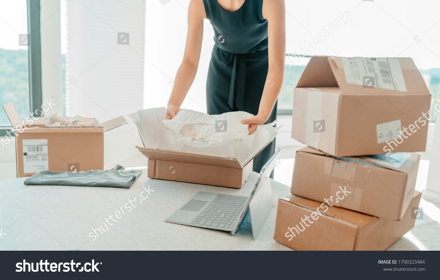 Selling clothing from home. Small business entrepreneur woman packing dress clothes in mailing box for shipping from online store. #1790323484