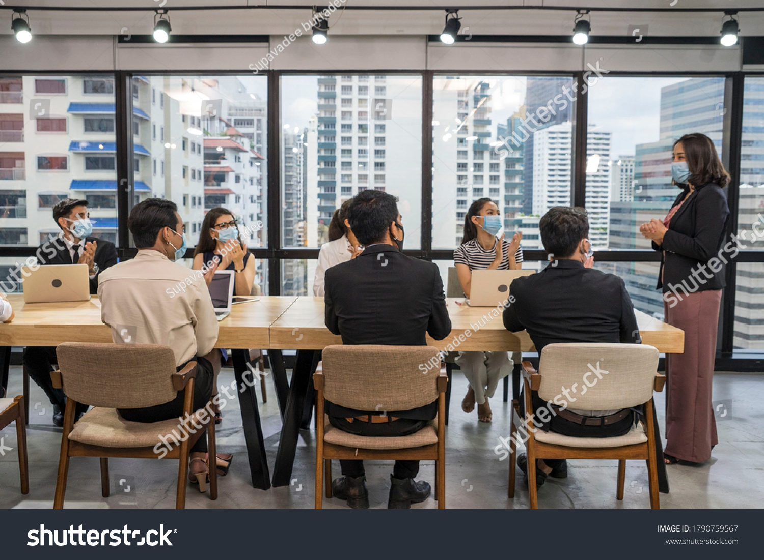 Group of employees sitting at a meeting, wearing a mask, having a leader standing at the head of the table in the meeting, introducing new normal work. #1790759567