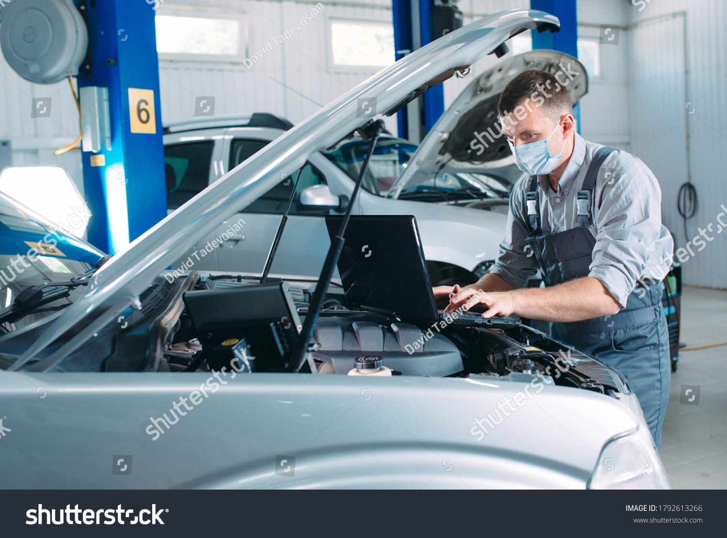 car mechanic using a computer laptop to diagnosing and checking up on car engines parts for fixing and repair #1792613266