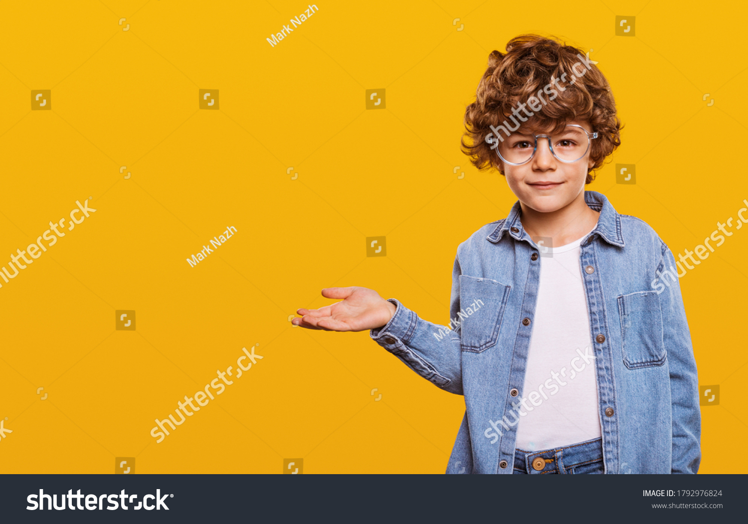 Cute child in denim shirt and glasses looking at camera and pointing at blank space isolated on yellow background #1792976824