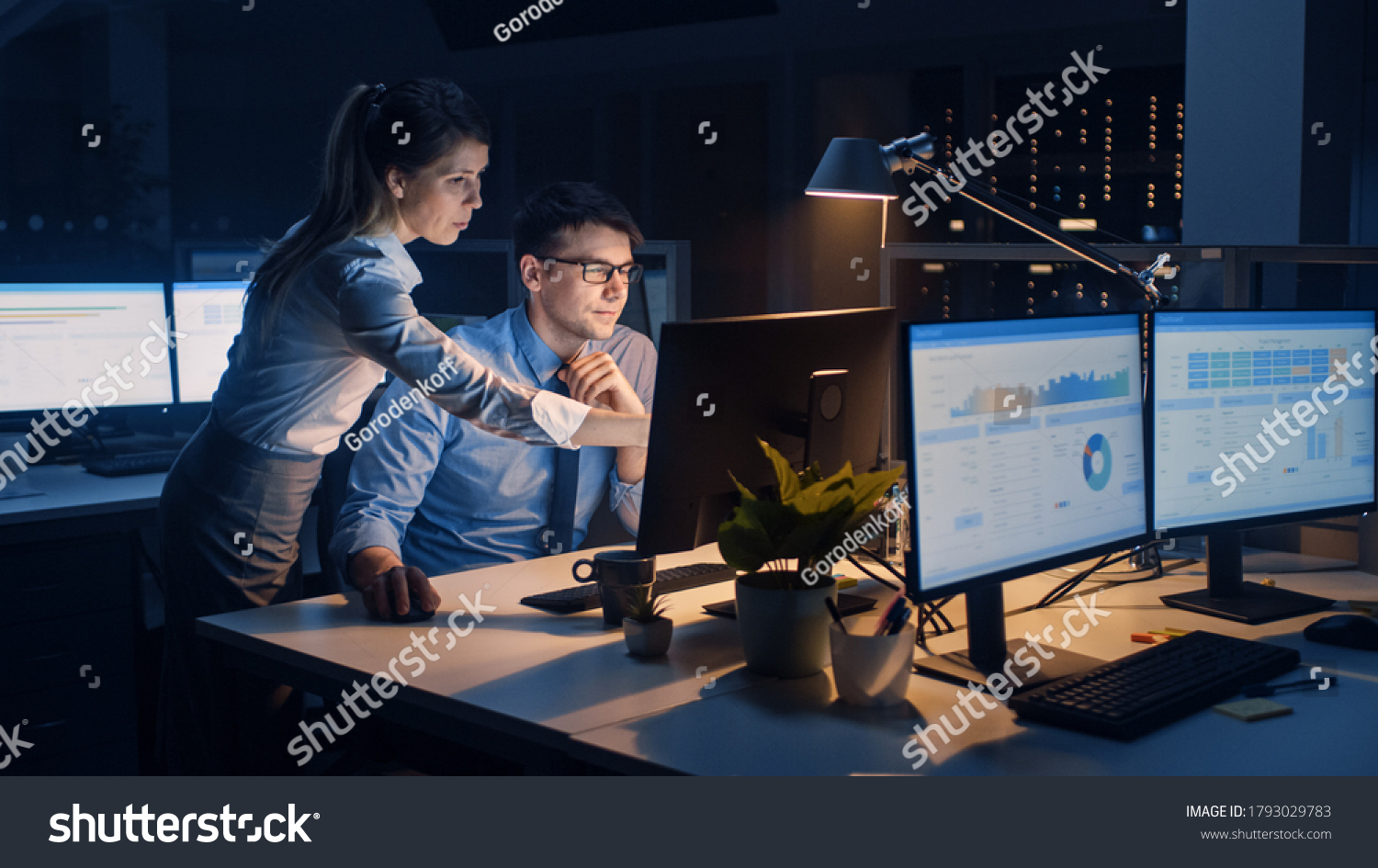 Businessman Uses Desktop Computer, His Female Project Manager Explains Specific Tasks, Account Handling and Strategic Moves. Professional People Late at Night in Big Corporate Office #1793029783