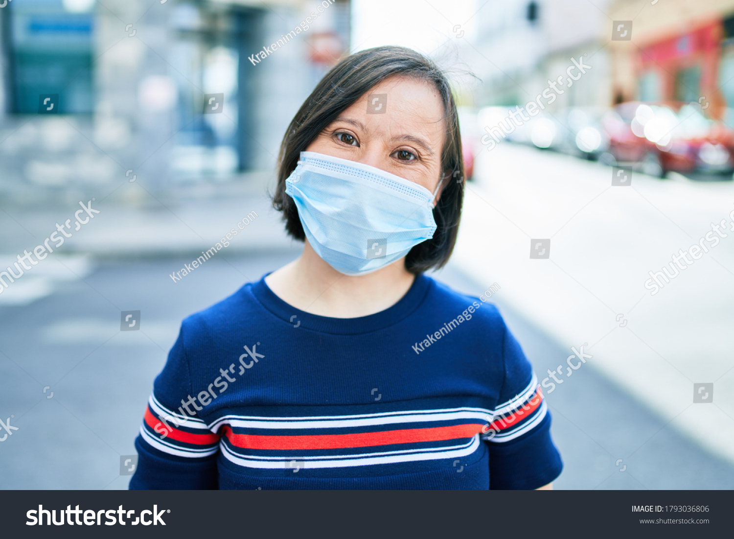 Beautiful brunette woman with down syndrome at the town on a sunny day wearing safety medical mask for coronavirus #1793036806