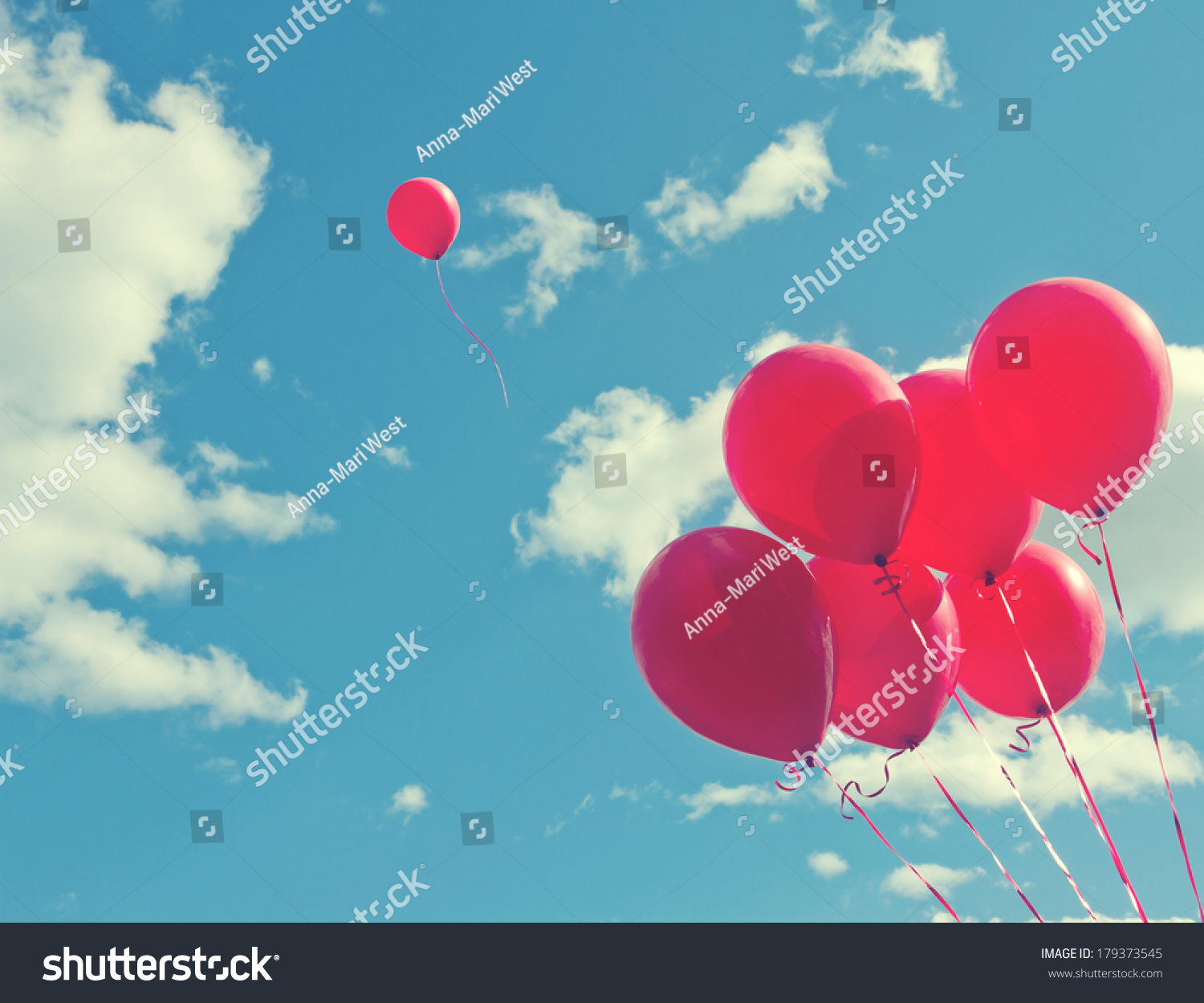 Bunch of red balloons on a blue sky with one balloon escaping to be individual and free - concept for following one's dreams #179373545
