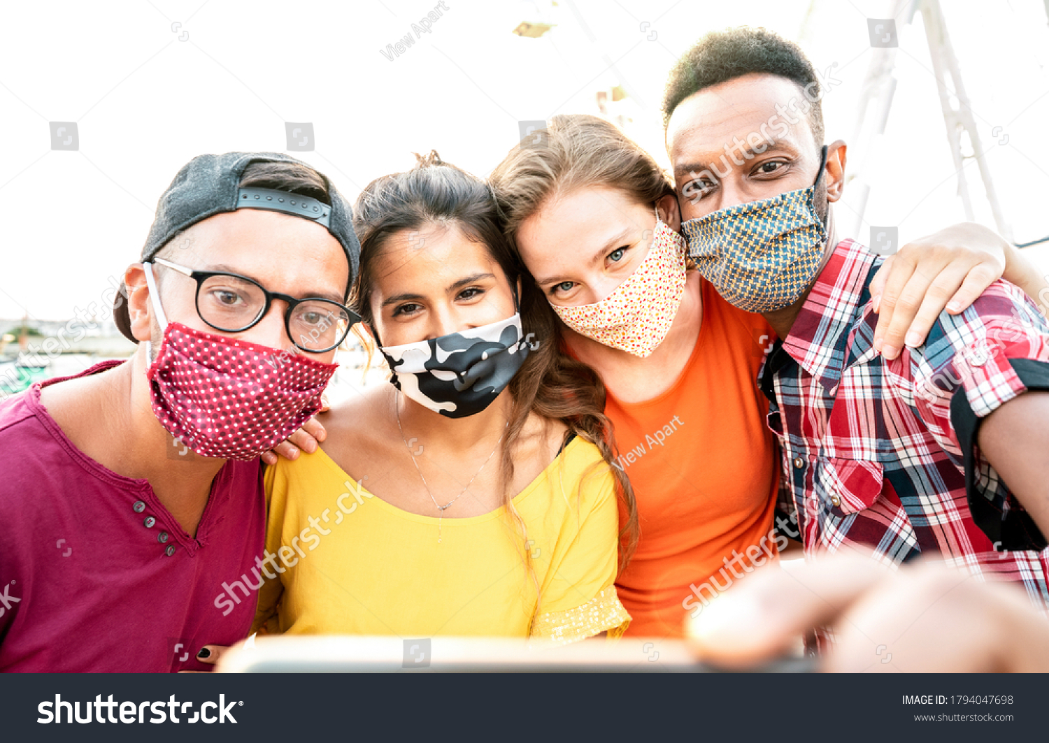 Multicultural milenial travelers taking selfie with closed face masks - New normal travel concept with young people having safe fun together at ferris wheel - Bright warm sunshine filter #1794047698