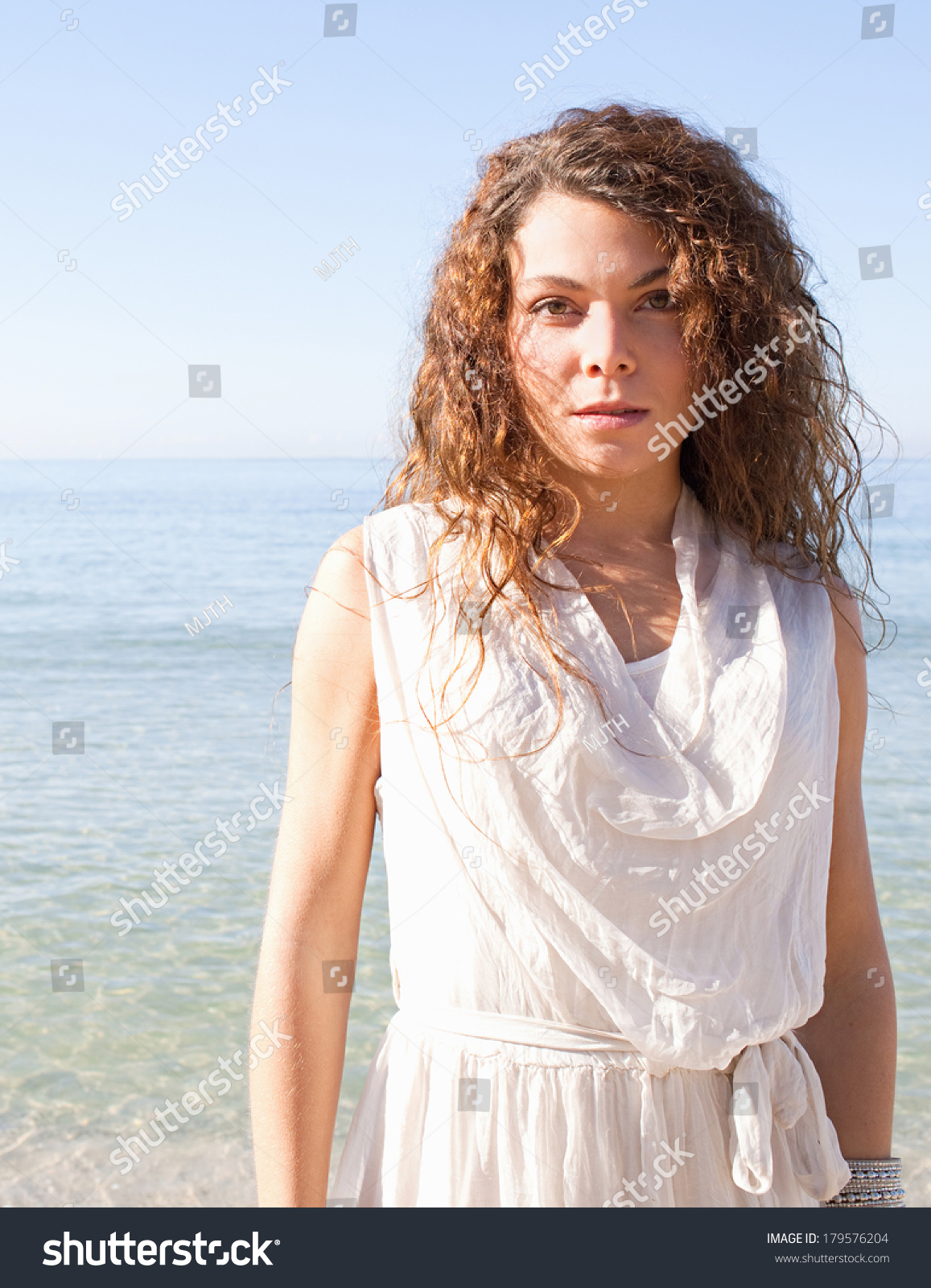 Portrait of a beautiful young woman standing and relaxing on a white sand beach with an intense blue sky on a summer holiday by the sea during a sunny day. Outdoors health and travel lifestyle. #179576204