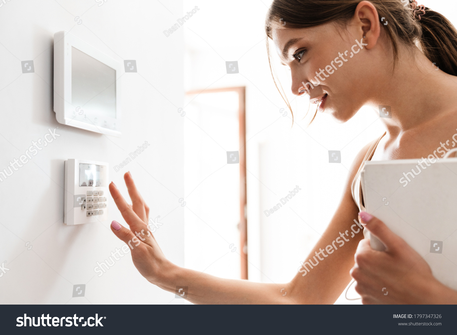 Young woman entering code on keypad of home security alarm #1797347326