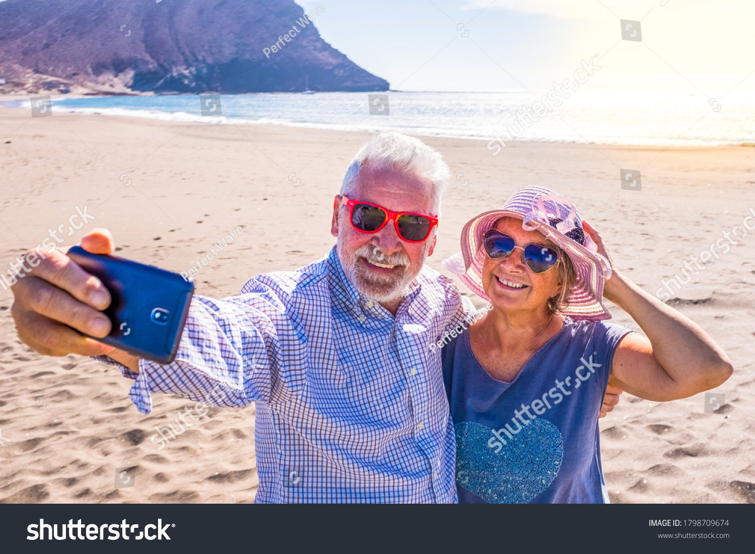 couple of mature people or pensioners enjoying their vacations and summer time together on the sand of the beach with the sea or ocean at the background - two retired senior taking a selfie smiling #1798709674