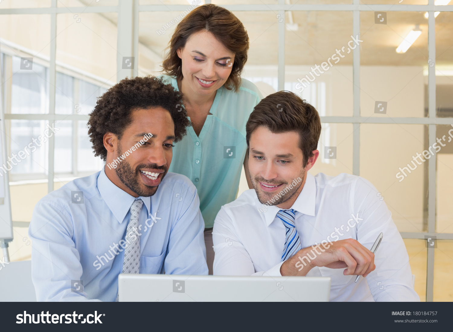 Three smiling young business people using laptop together at office #180184757