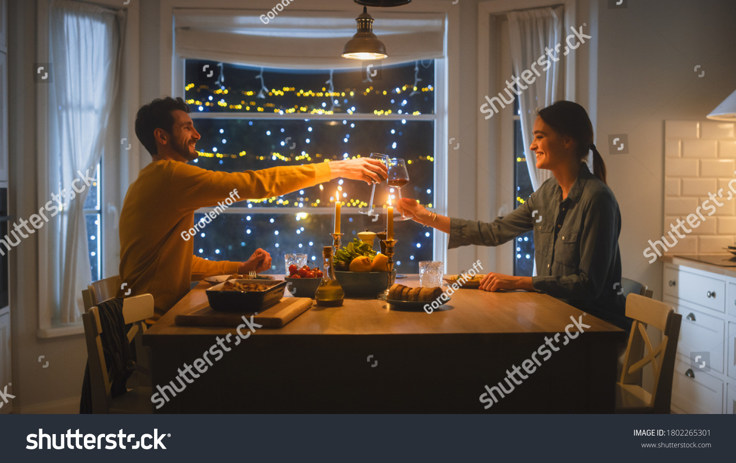 Happy Young Couple in Love Have Romantic Dinner, Toasting Each other with Glasses of Wine, Eating Tasty Meal in the Kitchen, Celebrating, Talking. Beautiful Lovely Husband and Wife Have Romantic Time #1802265301