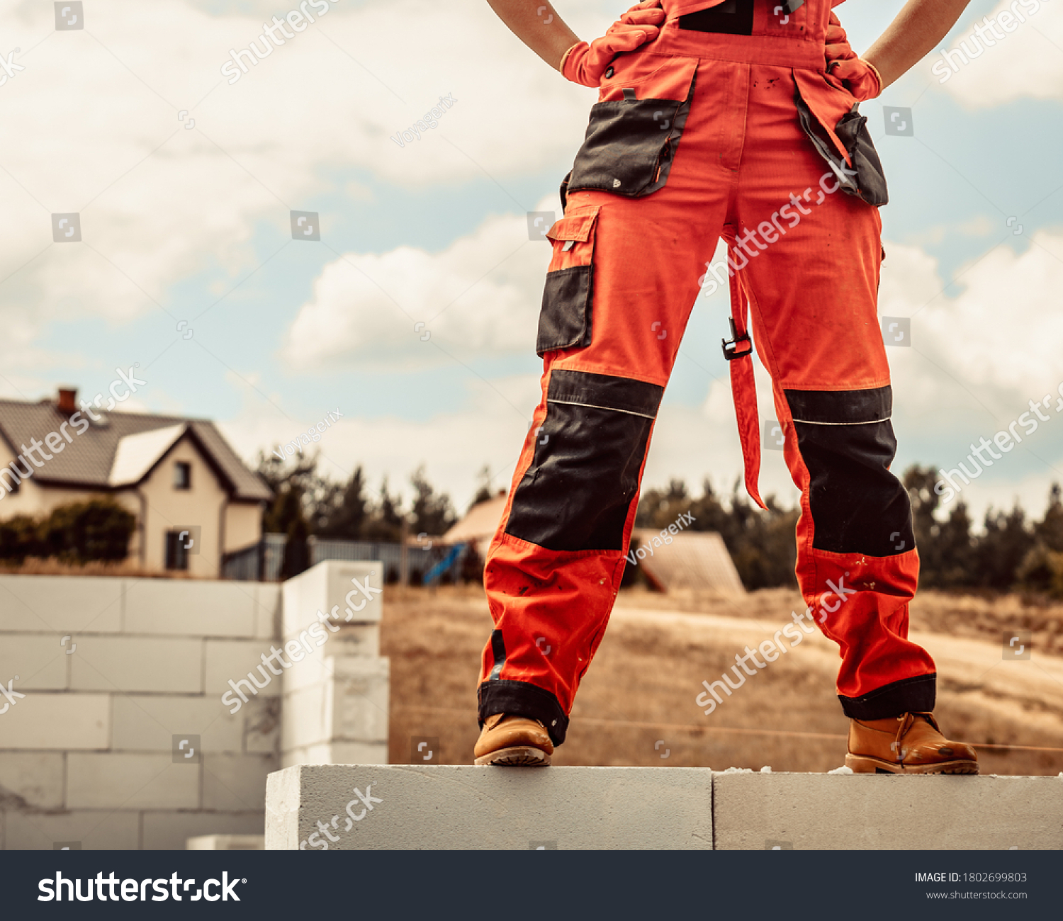 Low section legs of construction worker wearing workwear trousers and brown leather work boots standing on airbrick wall. #1802699803