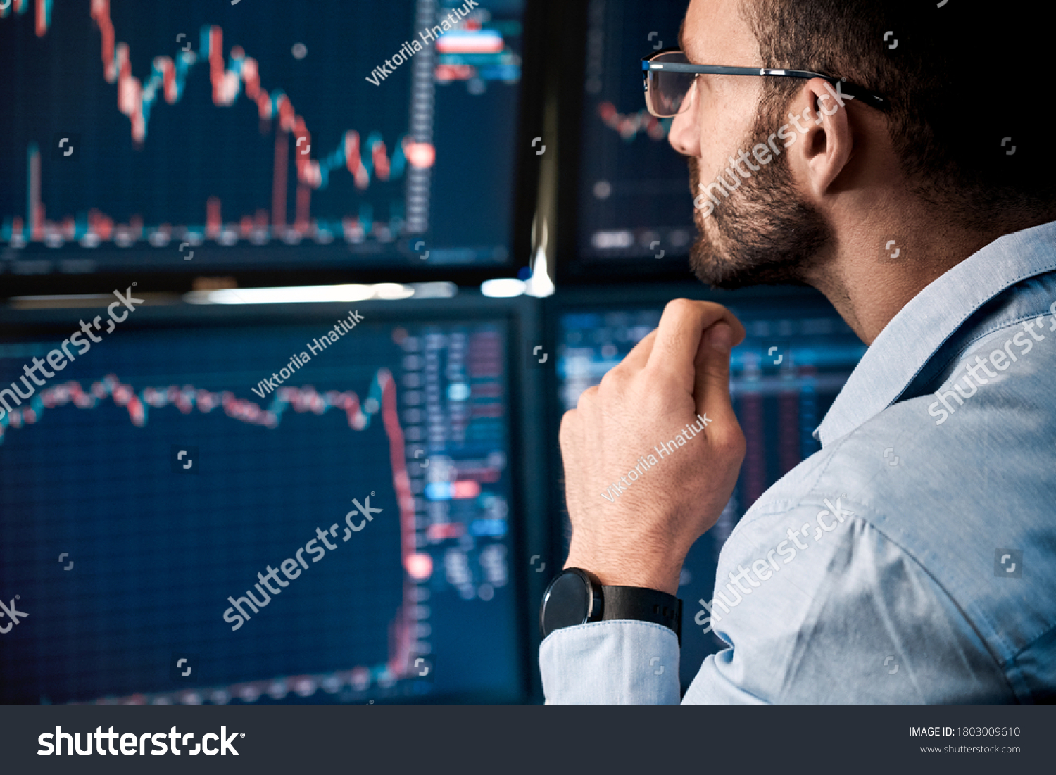 Bearded man trader wearing eyeglasses sitting at desk at office monitoring stock market looking at monitors analyzing candle bar price flow touching chin concerned trading concept close-up #1803009610