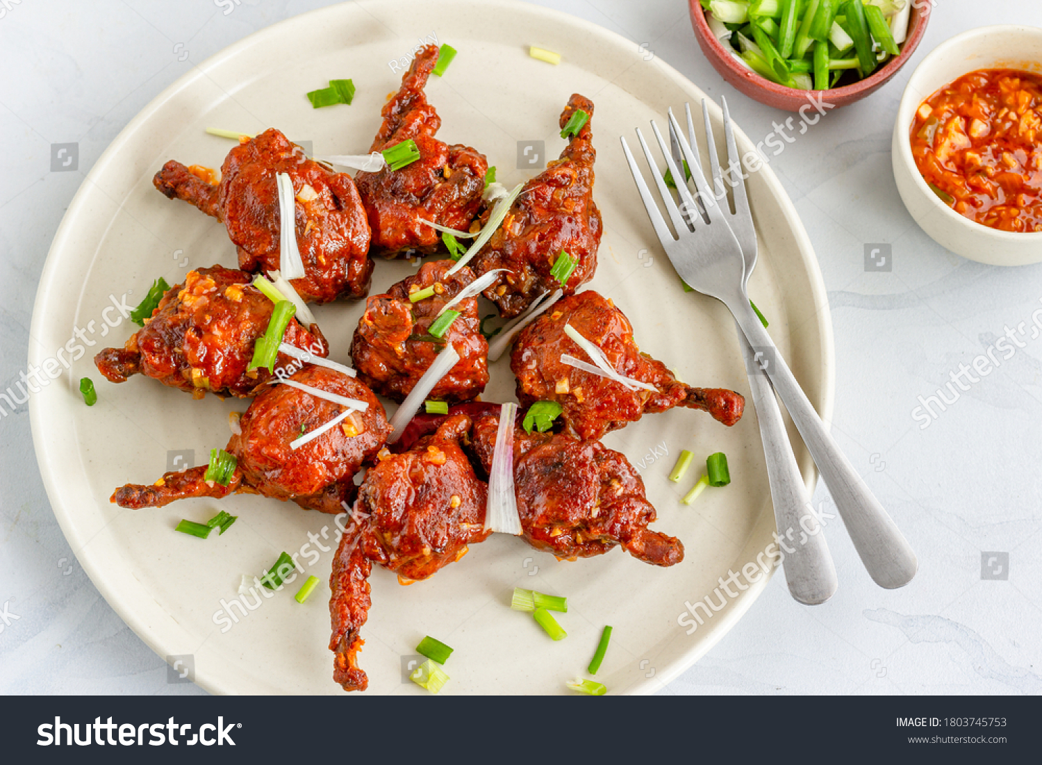 Popular Indo-Chinese Chicken Appetizer Made of Chicken Winglets on a White Plate on White Background Garnished with Scallion and Red Chili Pepper Horizontal Top View Photo #1803745753